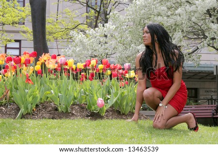 a sexy African American woman crouching near colorful red and yellow flowers