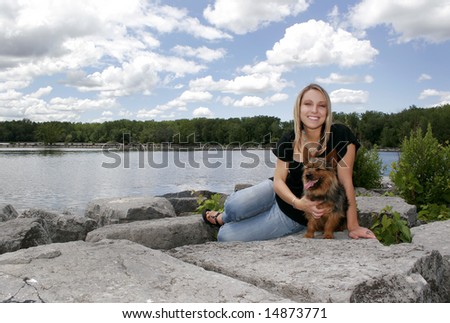 a blonde haired girl holding her dog near the water in a park