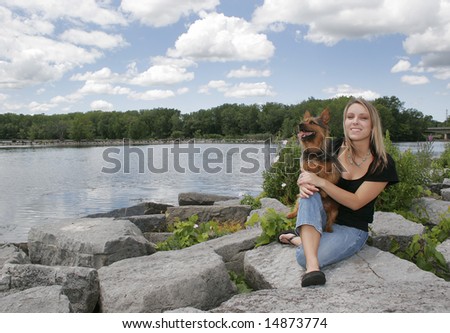 a blonde haired girl holding her dog near the water in a park