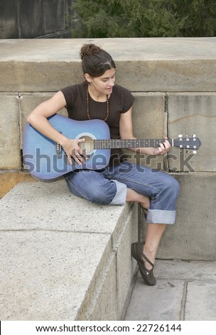one brunette attractive woman playing a blue guitar outside on a cement seat