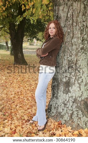 one young attractive redhead woman leaning against a tree in the fall