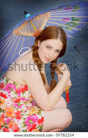 Teenage girl crouches and holds a flowered parasol while looking at the camera. Vertical format.