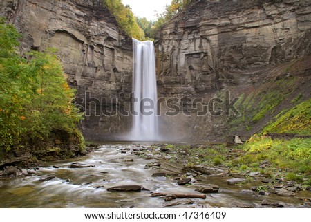 a tall natural waterfall falling over a tall mountain and into the river