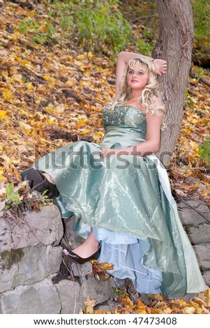 one pretty young blonde in a teal green prom dress sitting on a rock in the woods