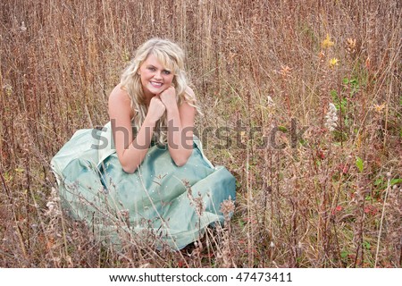 one pretty young blonde in a teal green prom dress sitting outdoors in a field