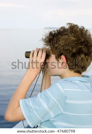 one young messy haired boy looking over a ship railing into the water with binoculars on a foggy day
