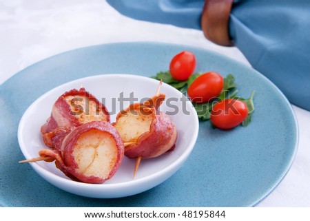 three delicious bacon wrapped scallops in a white bowl with tomato and oregano garnish on a blue plate