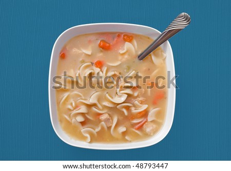 one large bowl of chicken noodle soup in a white bowl over a blue tablecloth background