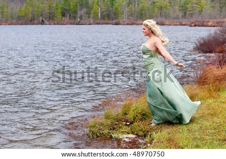 young teen blonde girl in a teal prom dress near the lake