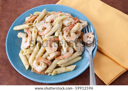 blue plate full of pesto shrimp pasta on a brown tablecloth