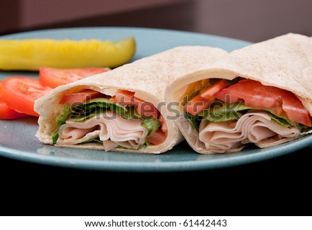 one sliced turkey wrap on a blue plate with pickles and tomatoes