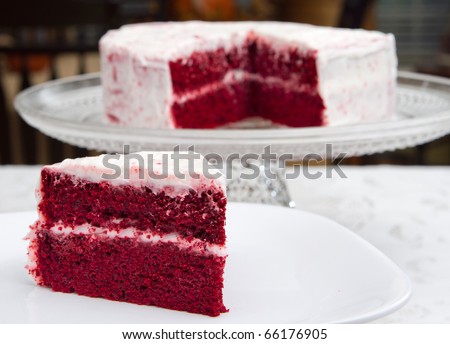 red velvet cake on a glass platter with one slice removed in front