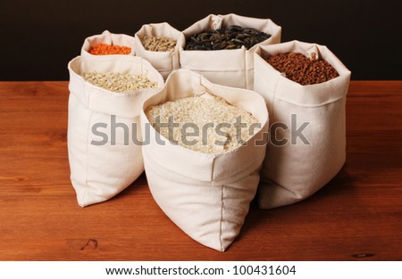 Cloth bags with grain on wooden table on brown background