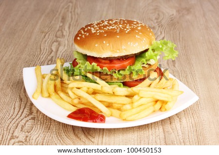 Big and tasty hamburger and fried potatoes on plate on wooden table