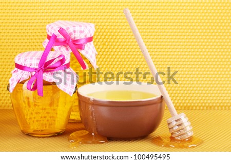 Jars of honey, bowl and wooden drizzler with honey on yellow honeycomb background