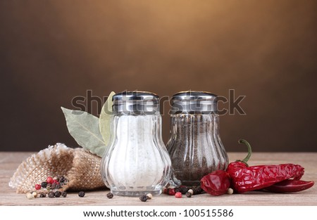 Salt and pepper mills and spices on wooden table on brown background