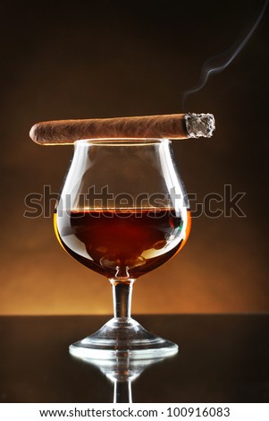glass of brandy and cigar on brown background