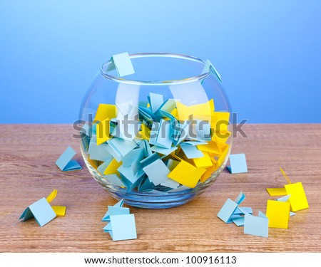 Pieces of paper for lottery in vase on wooden table on blue background
