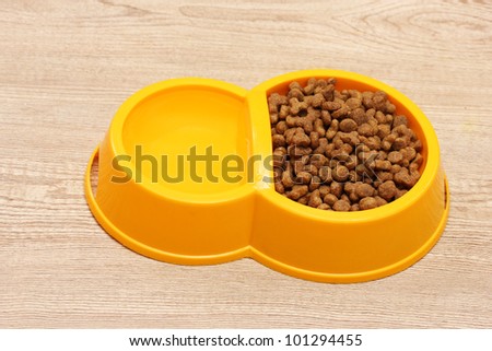 dry cat food and water in yellow bowl on wooden background