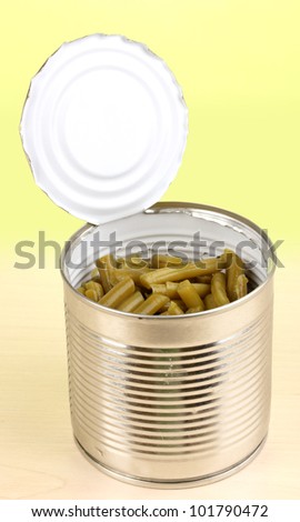 Open tin can of french bean on wooden table on green background