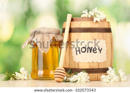 Sweet honey in barrel and jar with acacia flowers on wooden table on green background