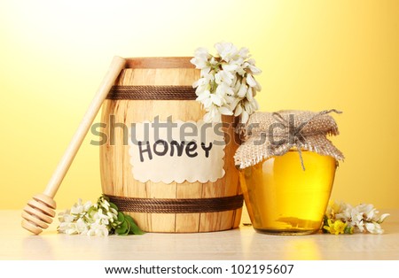 Sweet honey in barrel and jar with acacia flowers on wooden table on yellow background