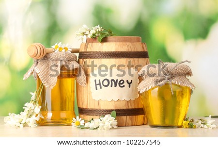 Sweet honey in barrel and jars with acacia flowers on wooden table on green background