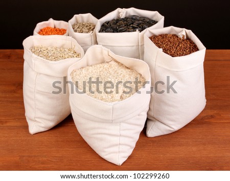 Cloth bags with grain on wooden table on brown background