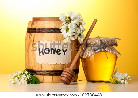 Sweet honey in barrel and jar with acacia flowers on wooden table on yellow background