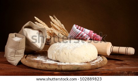 Dough and bags with flour on wooden table on brown background