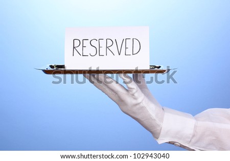 Hand in glove holding silver tray with card saying reserved on blue background