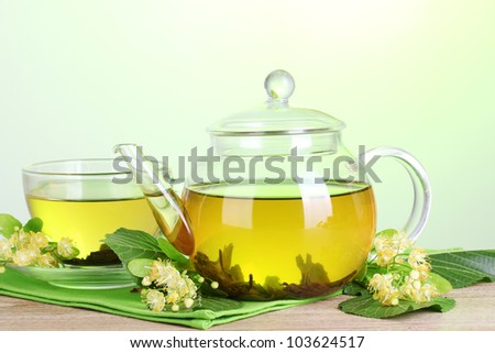 teapot and cup with linden tea and flowers on wooden table on green background