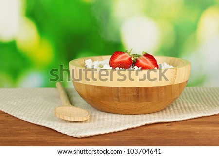 cottage cheese with strawberry in wooden bowl with wooden spoon on beige napkin on wooden table on green background