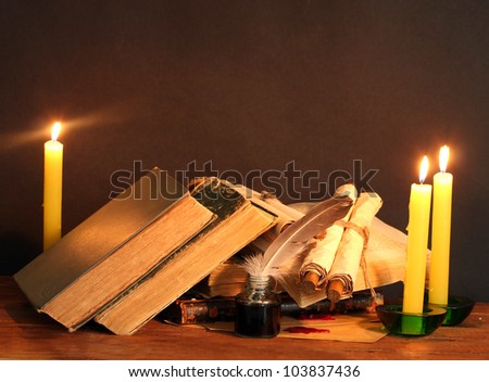 old books, scrolls, feather pen inkwell and candles on wooden table on brown background