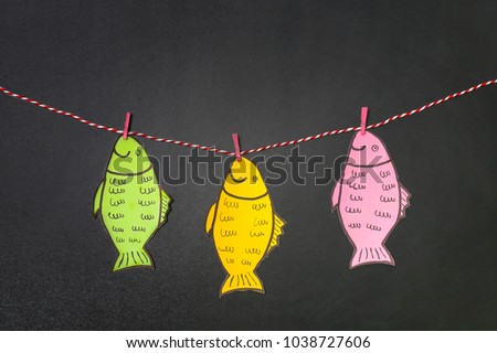 Paper fish hanging on string near chalkboard. April fool\'s day celebration