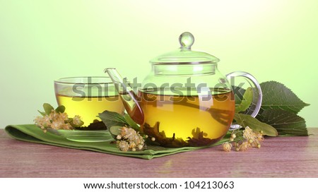 teapot and cup with linden tea and flowers on wooden table on green background