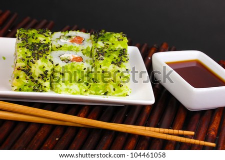 Tasty rolls served on white plate with chopsticks on bamboo mat on black background