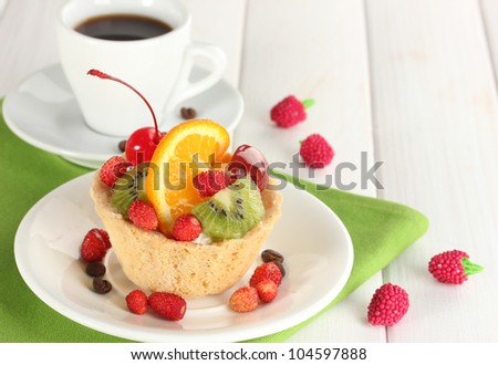 sweet cake with fruits on plate and cup of coffee on wooden table