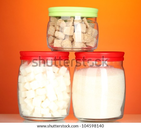 Jars with brown cane sugar lump, white crystal sugar and white lump sugar on colorful background