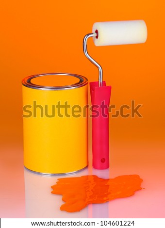 Can of paint with paint roller on colorful orange background