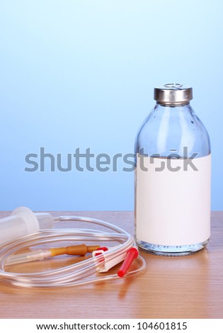 Bottle of intravenous antibiotics and plastic infusion set on wooden table on blue background