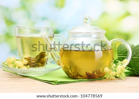 teapot and cup with linden tea and flowers on wooden table in garden