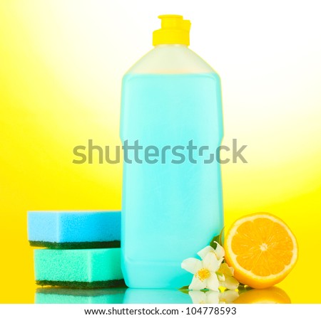 Dishwashing liquid with sponges and lemon with flowers on yellow background