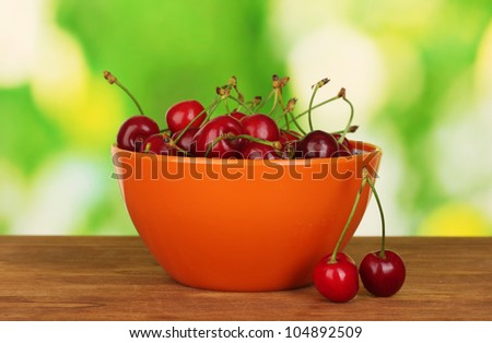 cherry in orange bowl on wooden table on green background