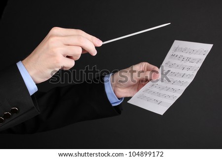 Music conductor hands with baton and notes isolated on black