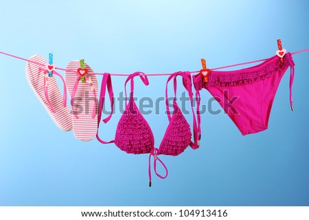 Women\'s swimsuit and flip-flops hanging on a rope on blue background