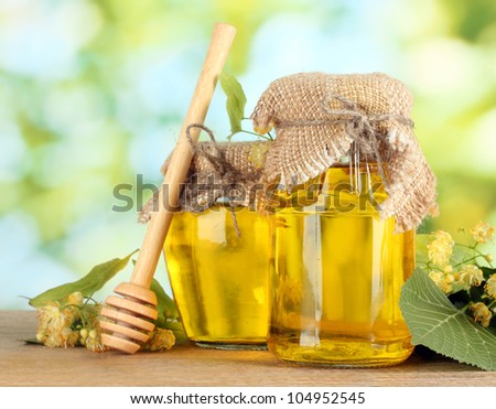 jars with linden honey and flowers on wooden table on green background