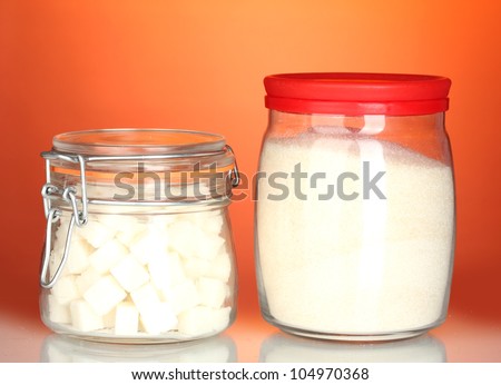 Jar with white crystal sugar and sugar-bowl with white lump sugar on colorful background