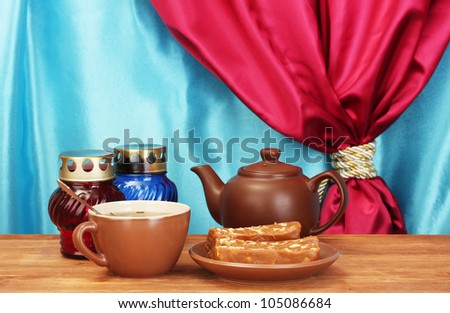 Teapot with cup and saucer with  sweet sherbet on wooden table on a background of curtain close-up