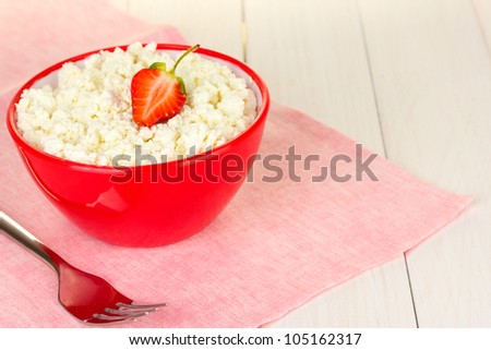 cottage cheese with strawberry in red bowl and fork on pink napkin on white wooden table close-up
